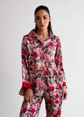A woman wearing a floral print silk sleepwear set, consisting of a button-up shirt and matching pants.